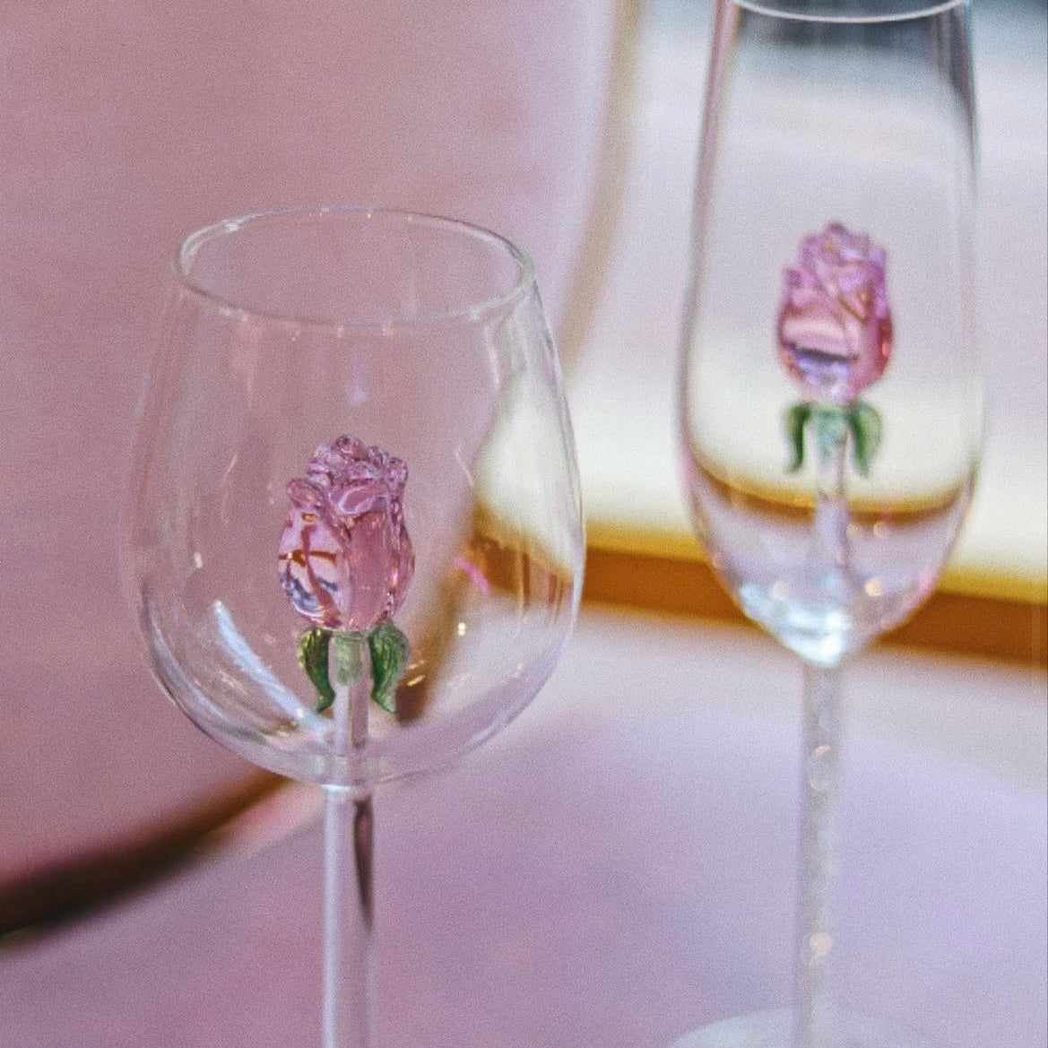 Two wine glasses with pink floral designs on a pink background